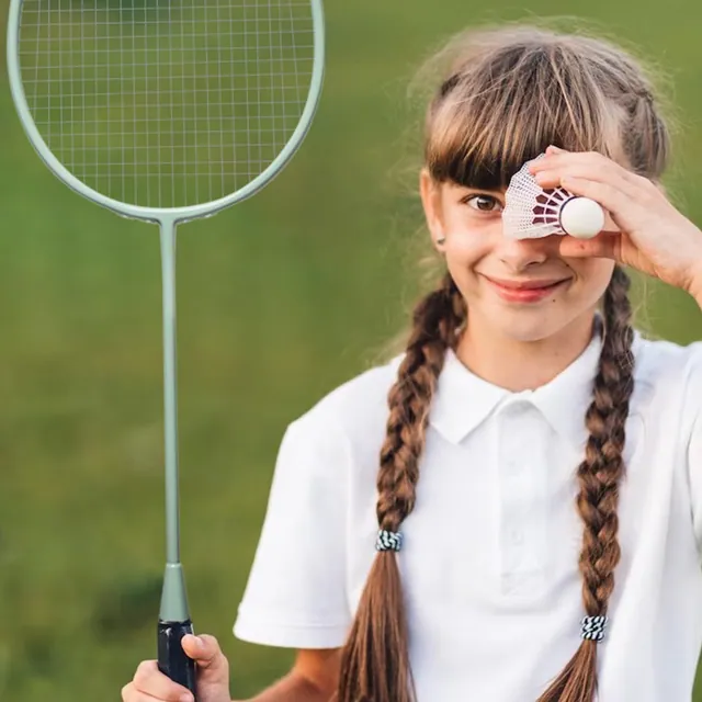 A girl with braids holding a shuttlecock up to her eye, racket in her other hand