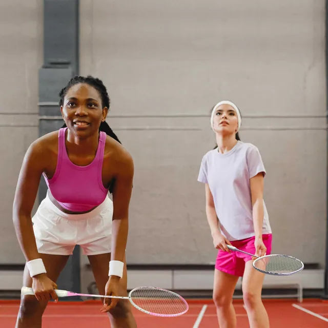 Two women ready to receive on an indoor badminton court