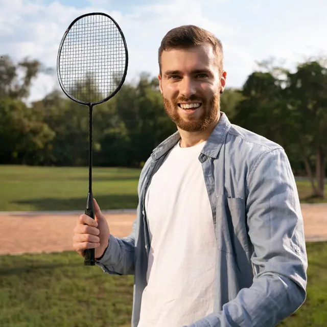 A smiling man holding a badminton racket in a park