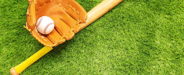 A leather glove holding a baseball on a bat wrapped in yellow grip tape, lying on grass