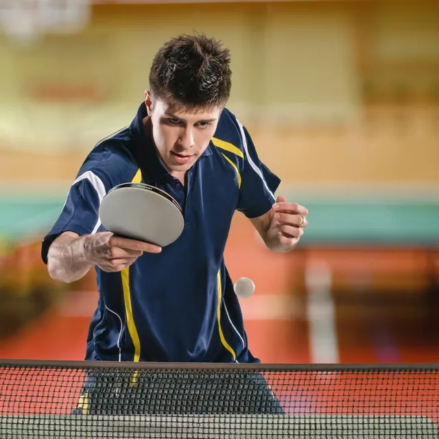 A young player leaning over the net to return a shot in an indoor hall