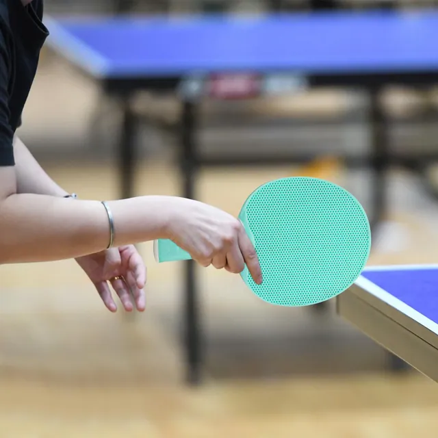 Hands holding a mint paddle at the edge of a blue table, ready to serve
