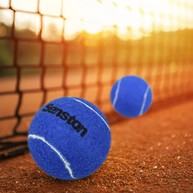 Two blue Senston tennis balls on a clay court beside the net at sunset