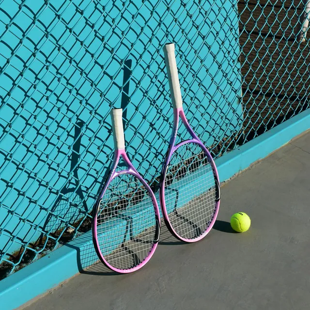 Two tennis rackets leaning on a teal court fence with a ball at their feet
